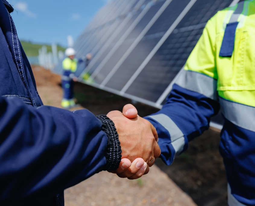 Partners Sharing A Handshake In Front Of Solar Panels